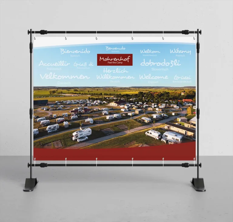 Willkommens-Banner des Mohrenhof Campingplatzes mit mehrsprachigen Grüßen und einer Luftaufnahme der Stellplätze.