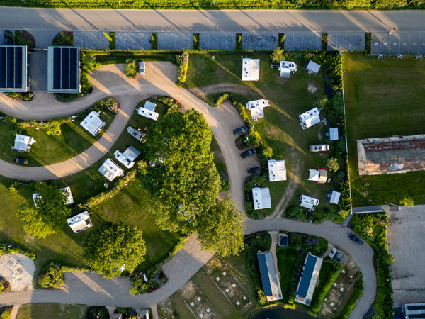 Luftaufnahme eines gepflegten Campingplatzes mit Stellplätzen für Wohnmobile und Wohnwagen im Grünen