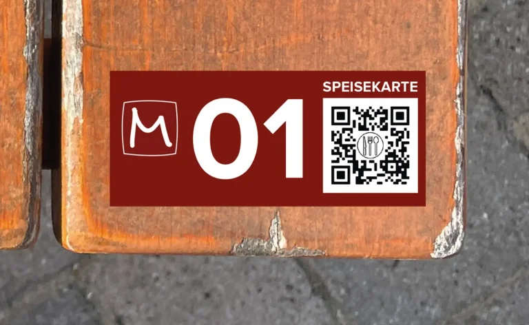 Tischnummernschild mit QR-Code zur Speisekarte, aufgeklebt auf der Holzleiste eines Biertisches.