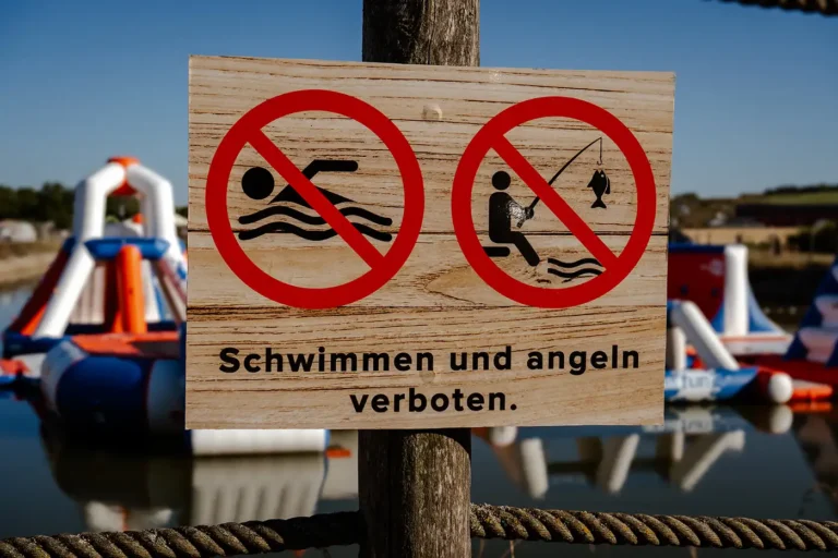 Warnschild aus Holz mit Verbotssymbolen für Schwimmen und Angeln vor dem Aquapark