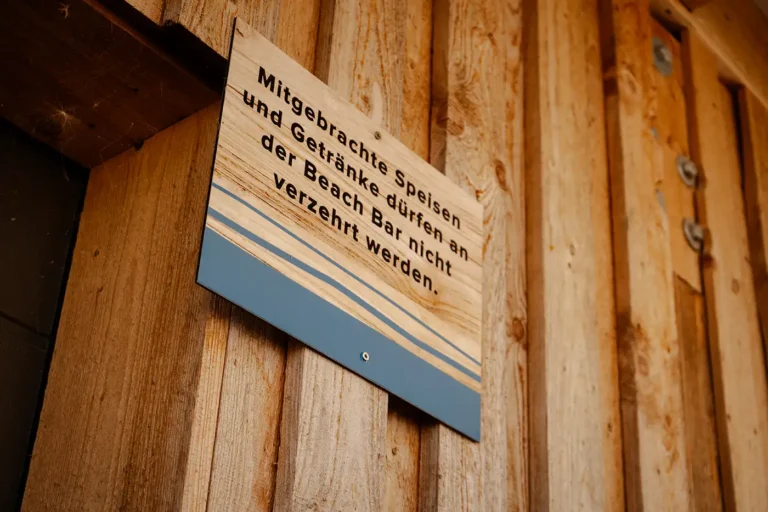 Holzschild mit Aufschrift: Mitgebrachte Speisen und Getränke dürfen an der Beach Bar nicht verzehrt werden